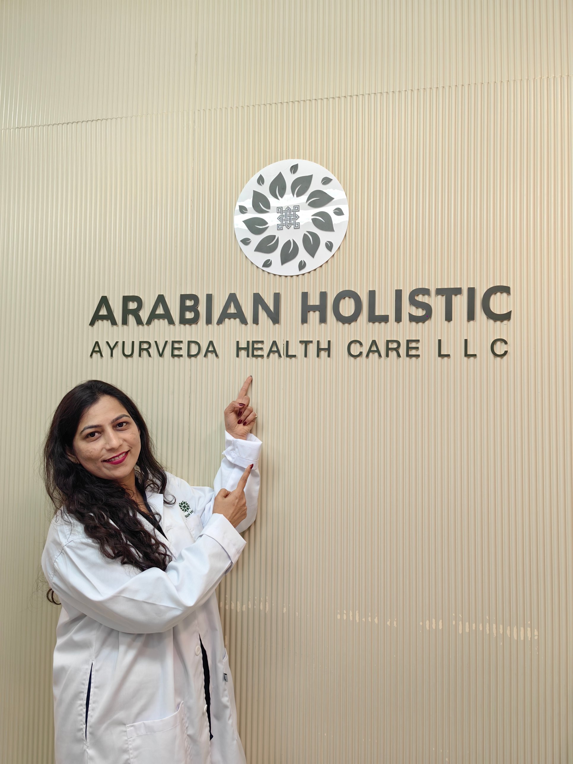 Member of the Arabian Holistic team in a white uniform pointing to the centre logo at reception